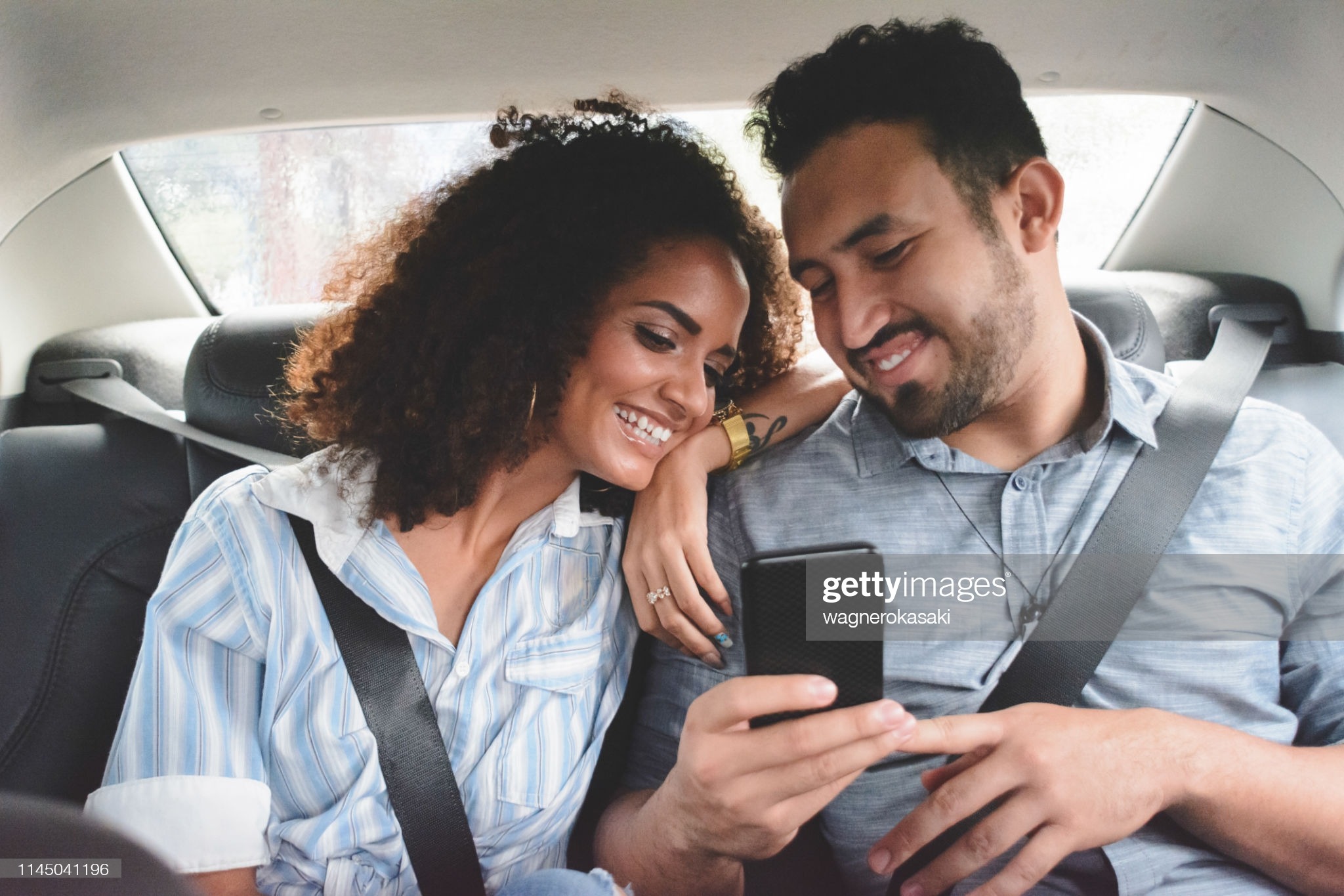 Young Couple Watching Something At Smartphone In The Backseat Of A Car